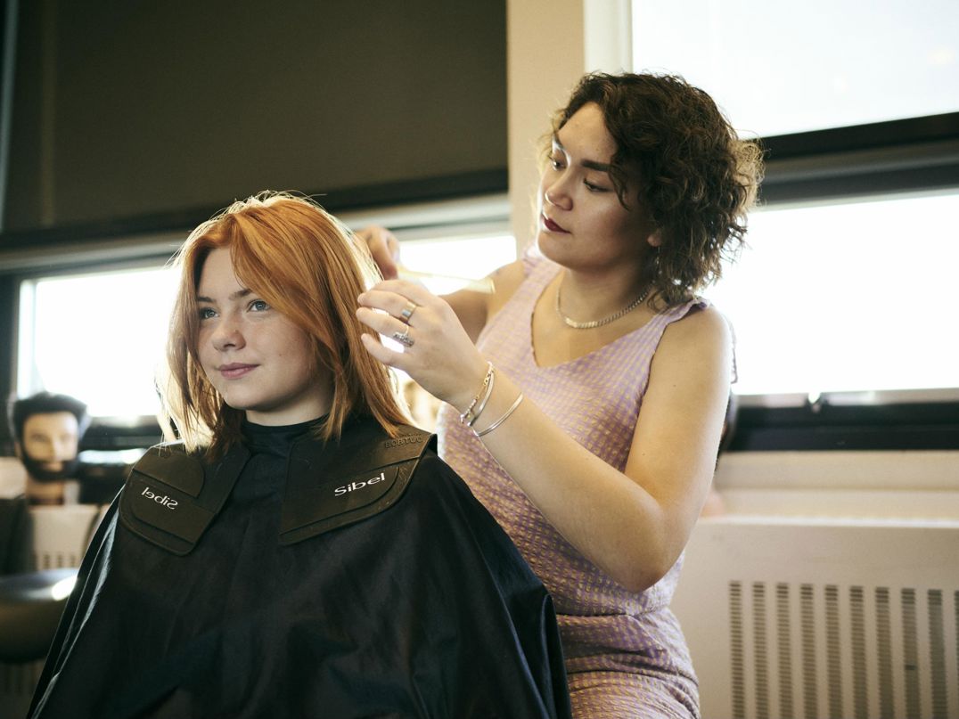 En pige sidder model og får ordnet håret af en frisørelev på Hansenberg.