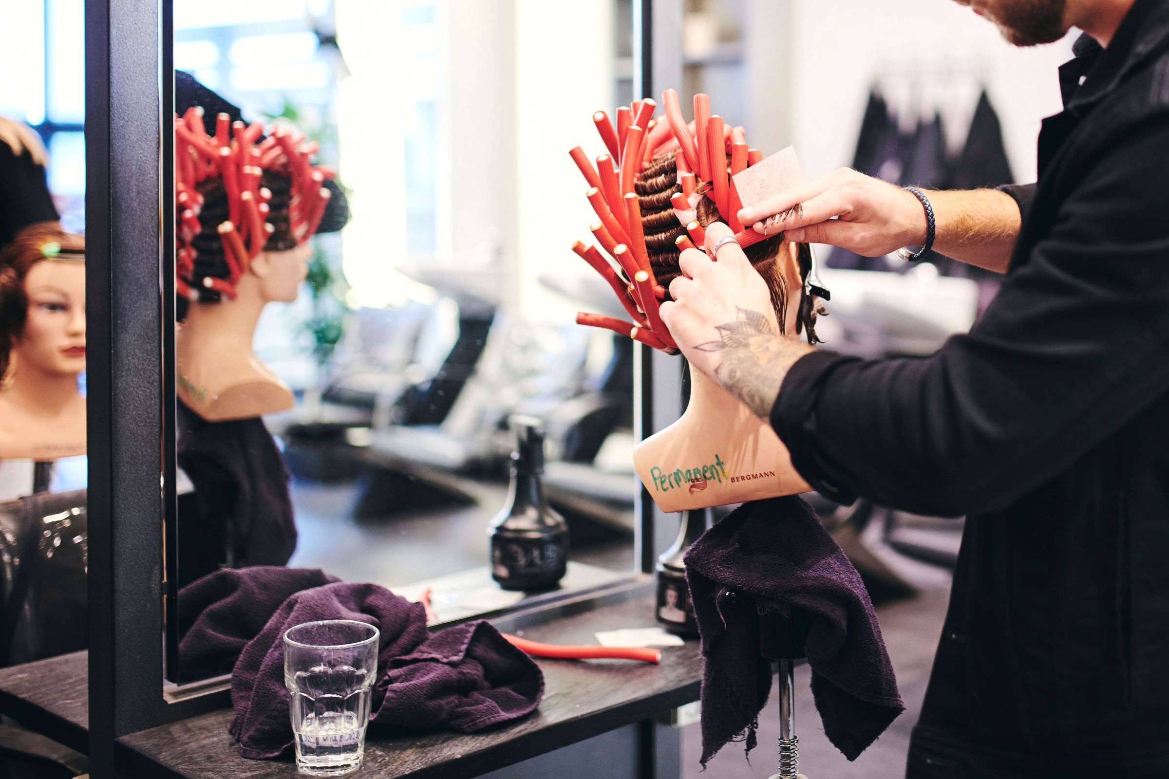 En mandlig frisørelev på Hansenberg ruller curlers i håret på et øvelseshoved.