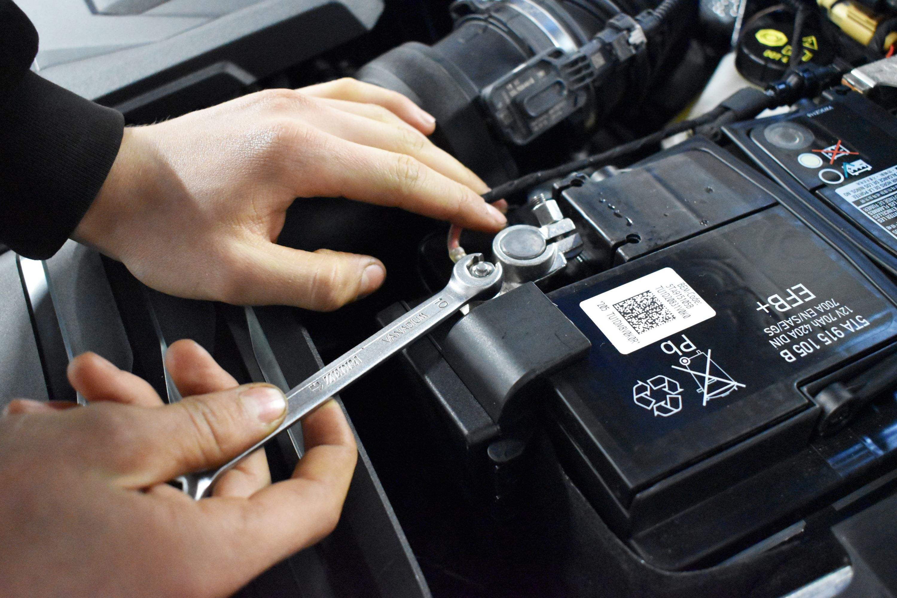 En mekanikerelev løsner en møtrik i en bilmotor.