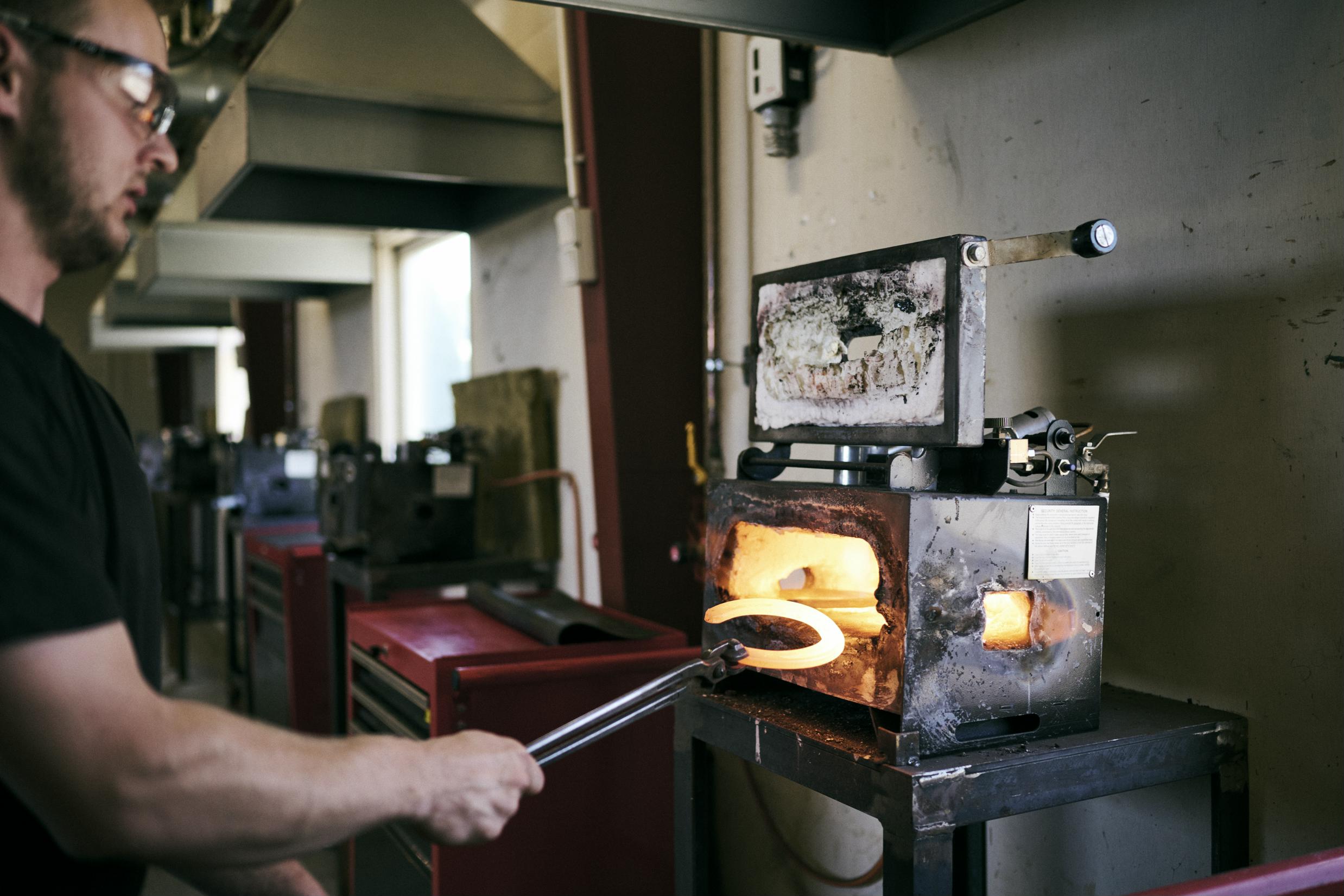 En beslagsmedelærling tager en gloende varm hestesko ud fra essen i skolens beslagsmedje.