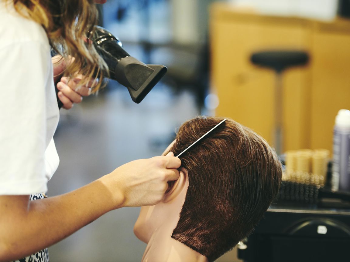 Frisørelev på Hansenberg tørrer og styler hår på et øvelseshoved i salonen