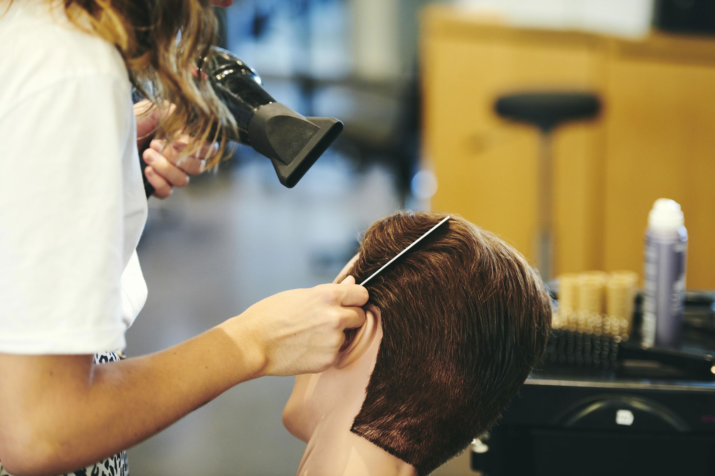 Frisørelev på Hansenberg tørrer og styler hår på et øvelseshoved i salonen