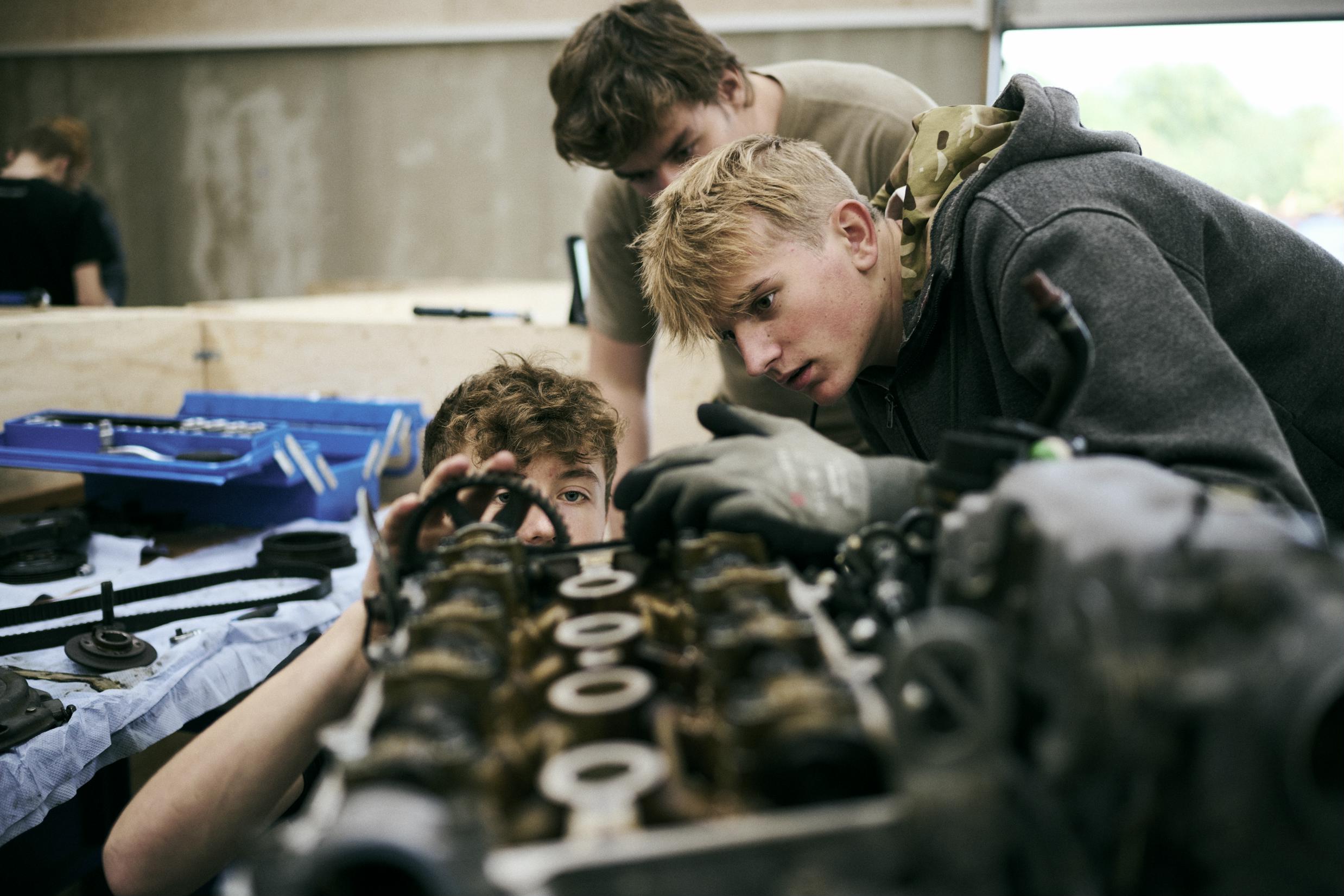Tre mekanikerelever på Grundforløb 1 nærstuderer en motor på et af skolens værksteder.