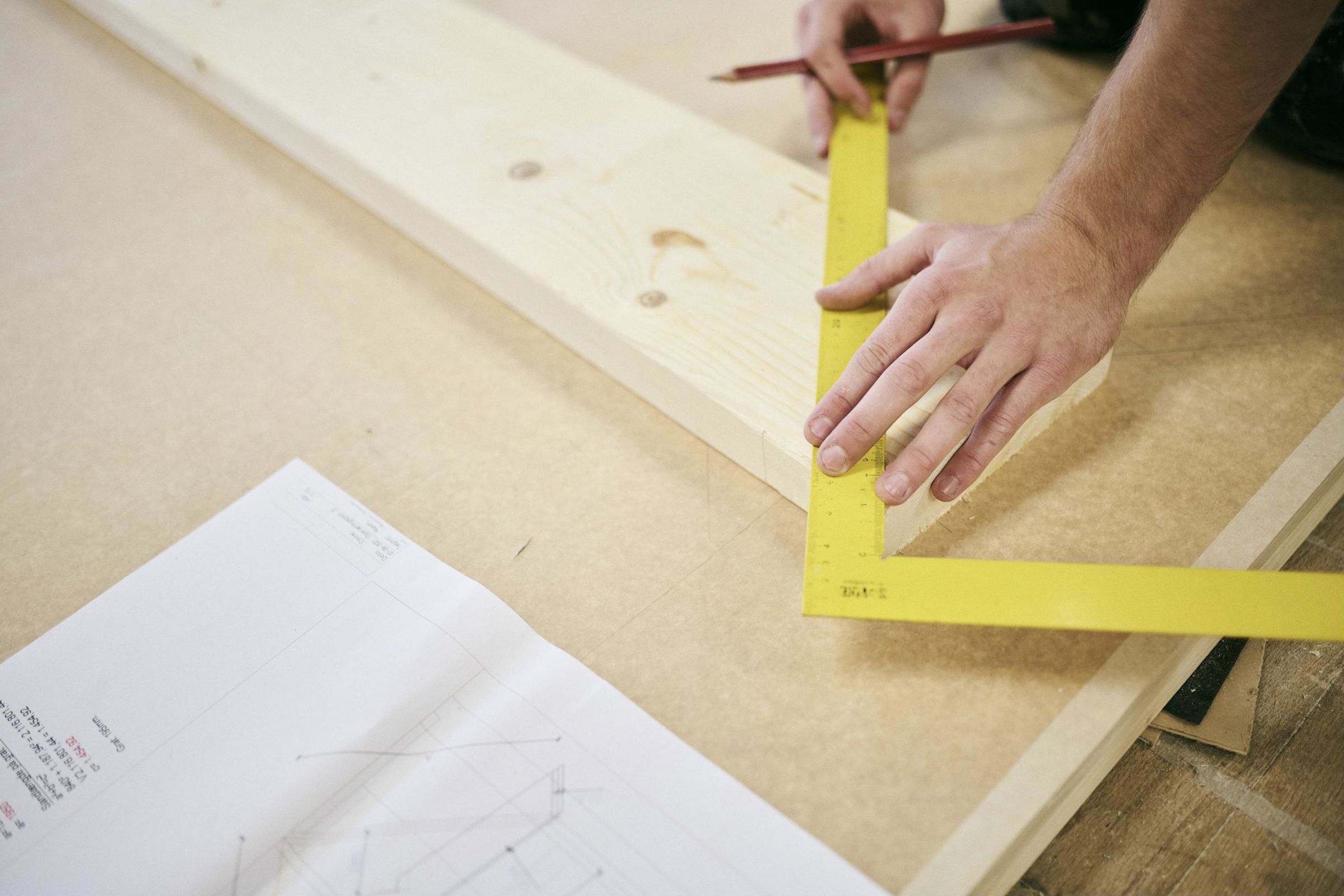 En tømrerlærling på Hansenbergs tømrerværksted måler og tegner op, så snittet, der skal saves, bliver præcist efter tegningen.