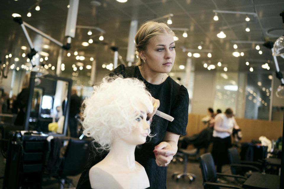 Frisørelev på Hansenberg retter på krøllerne på et øvelseshoved