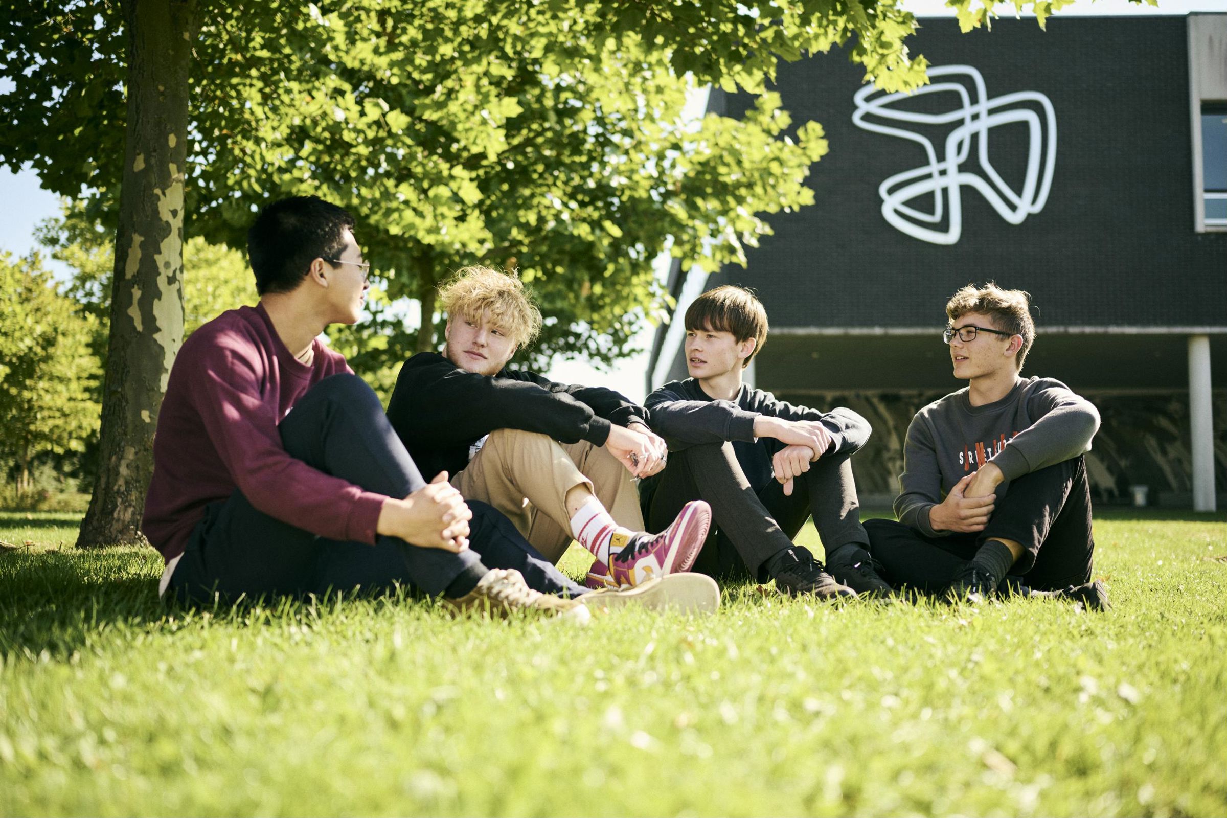 4 HTX-elever nyder det gode vejr i pausen ude foran Hansenberg Tekniske Gymnasium.