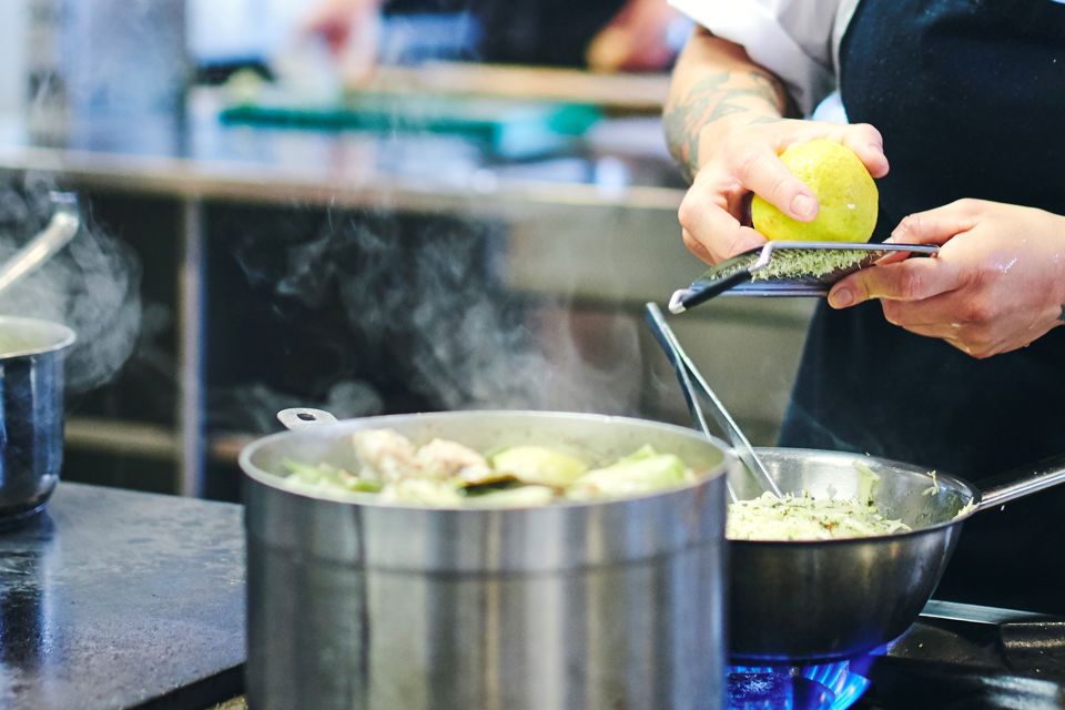 En kokkeelev tilsætter retten, der simrer over komfuret, noget friskrevet citronskal.
