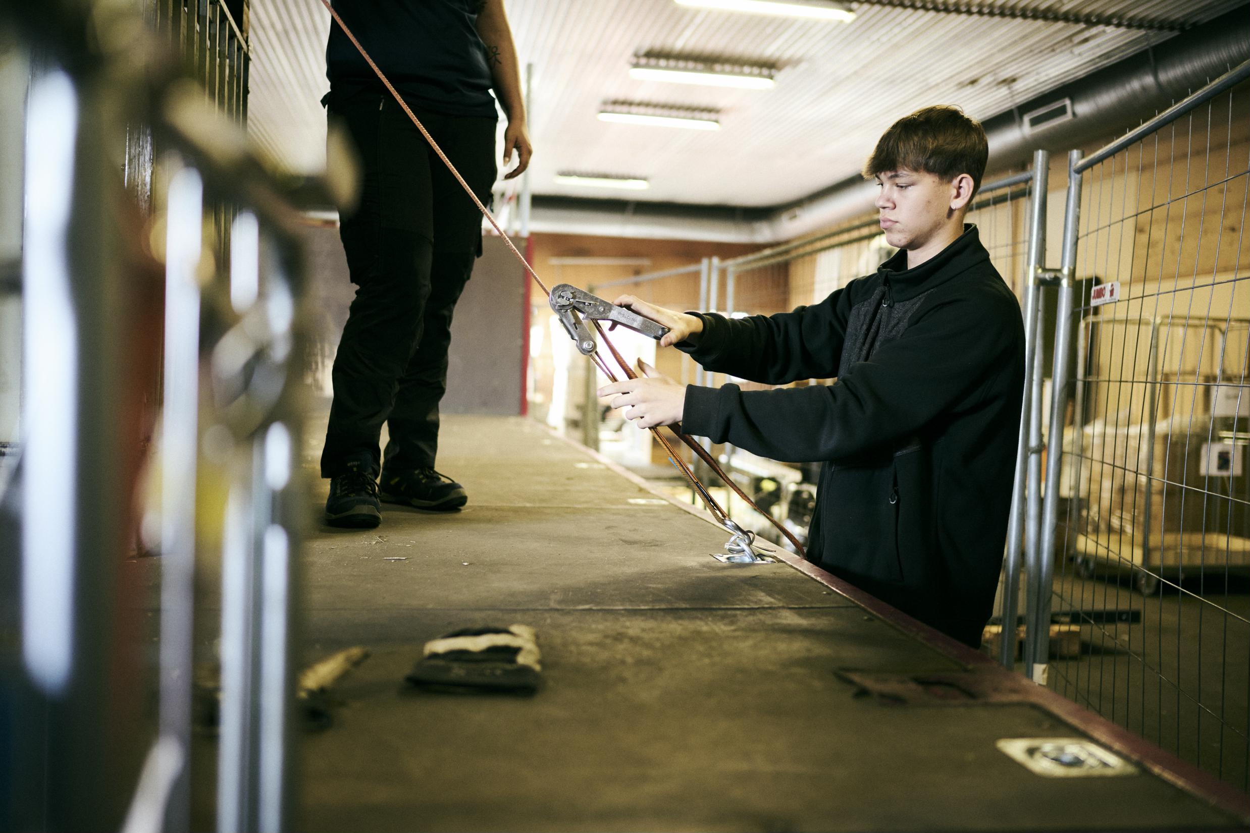 En elev på vejgodstransportuddannelsen er ved at surre godset fast på ladet af en lastbil.