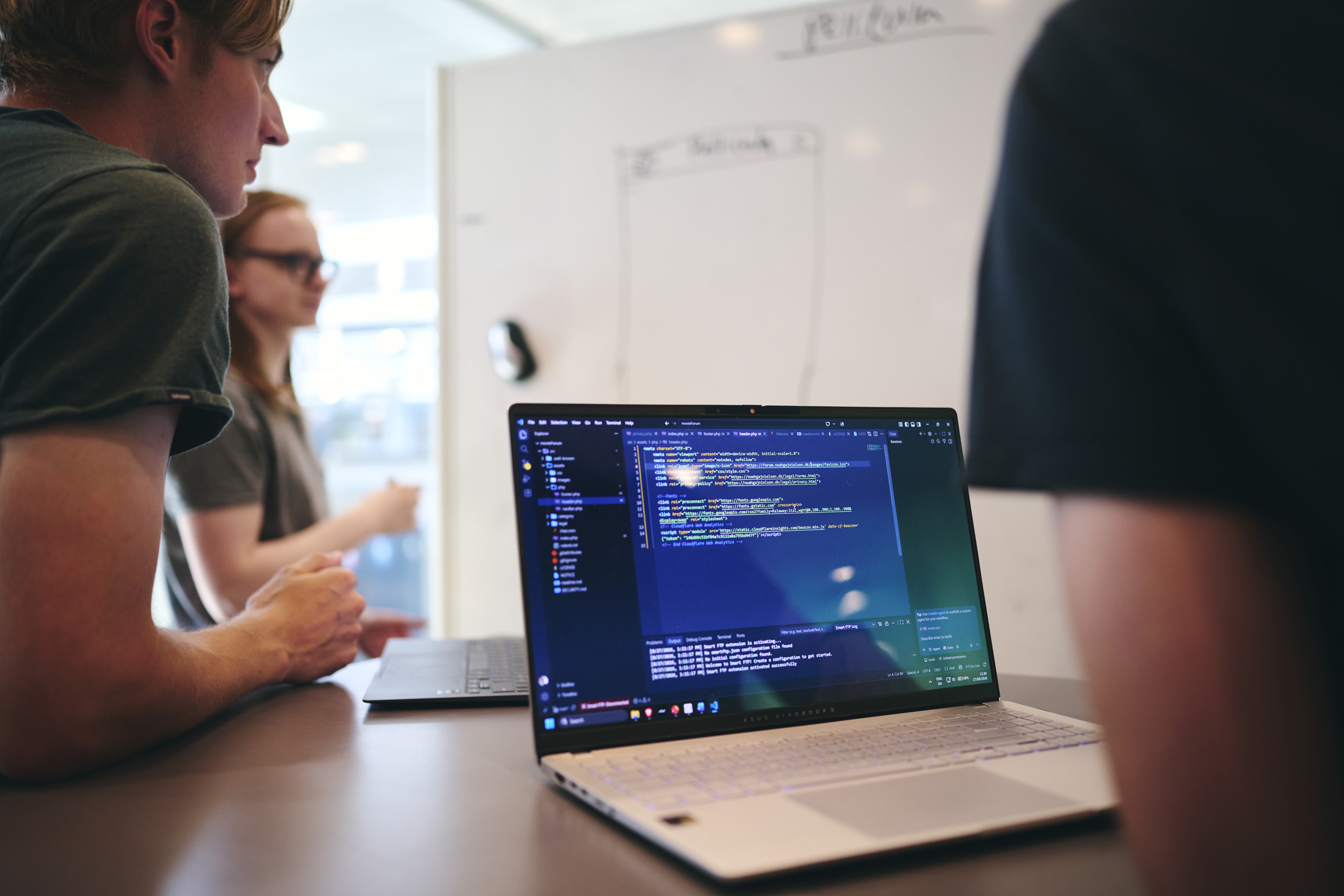 Tre elever på Hansenberg Tekniske Gymnasium har gruppearbejde i faget programmering, man kan se både en hvid tavle og en bærbar med koder på skærmen.