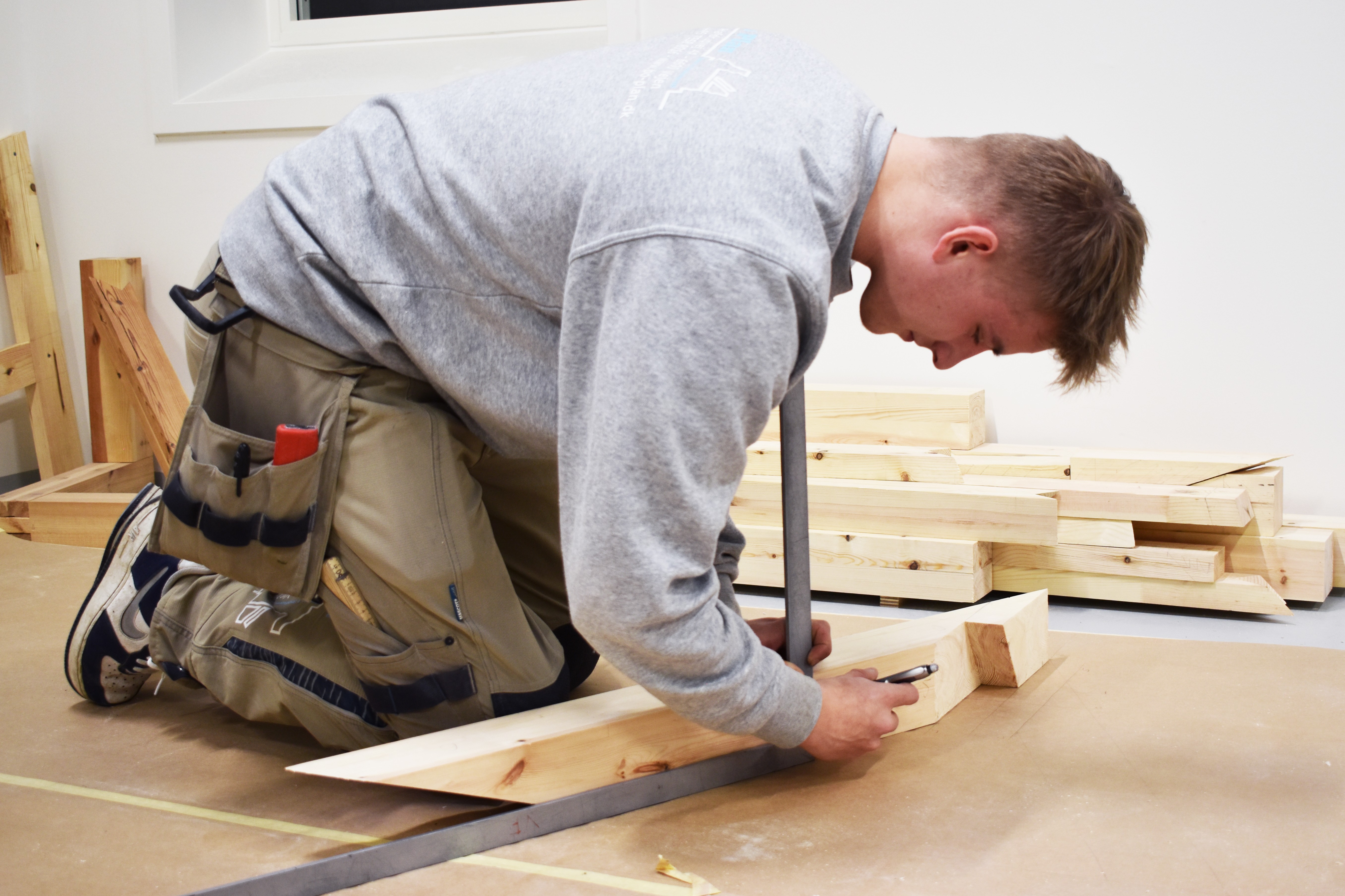 Toke, der er tømrerelev træner til DM i Skills 2024, og tjekker om målene på træet stemmer med tegningerne.