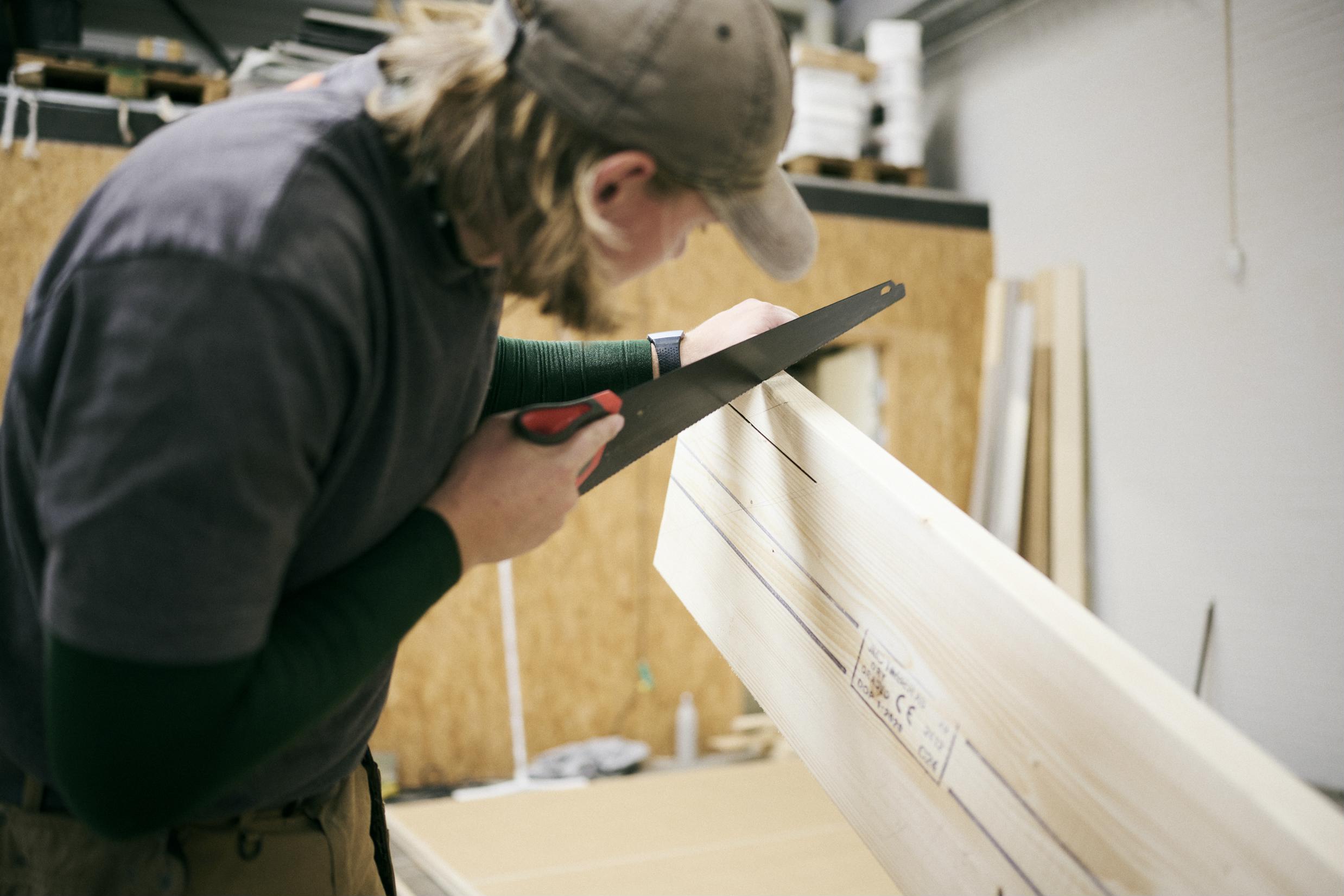 En tømrerelev lægger an til at save i et bræt.