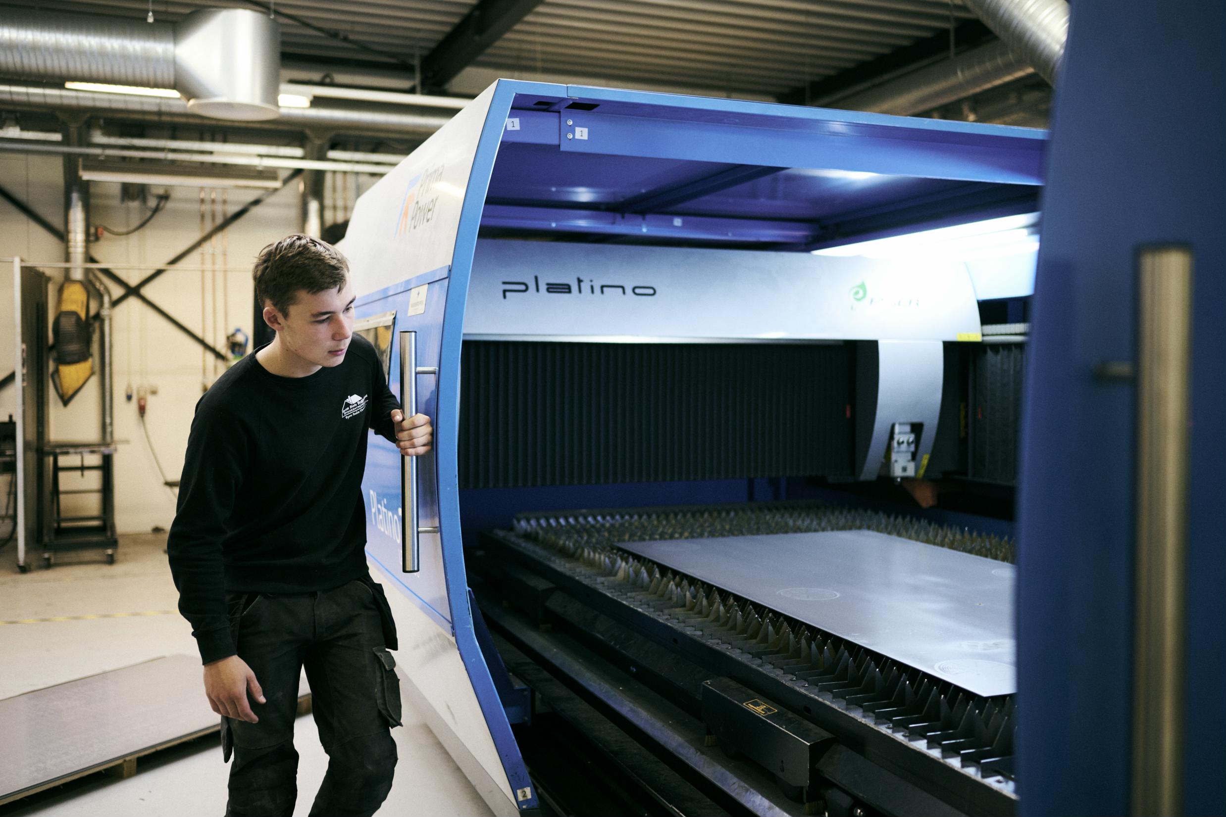 En smedeelev lukker skydedøren ind til den store fiberlaser på Hansenbergs smedeværksted.