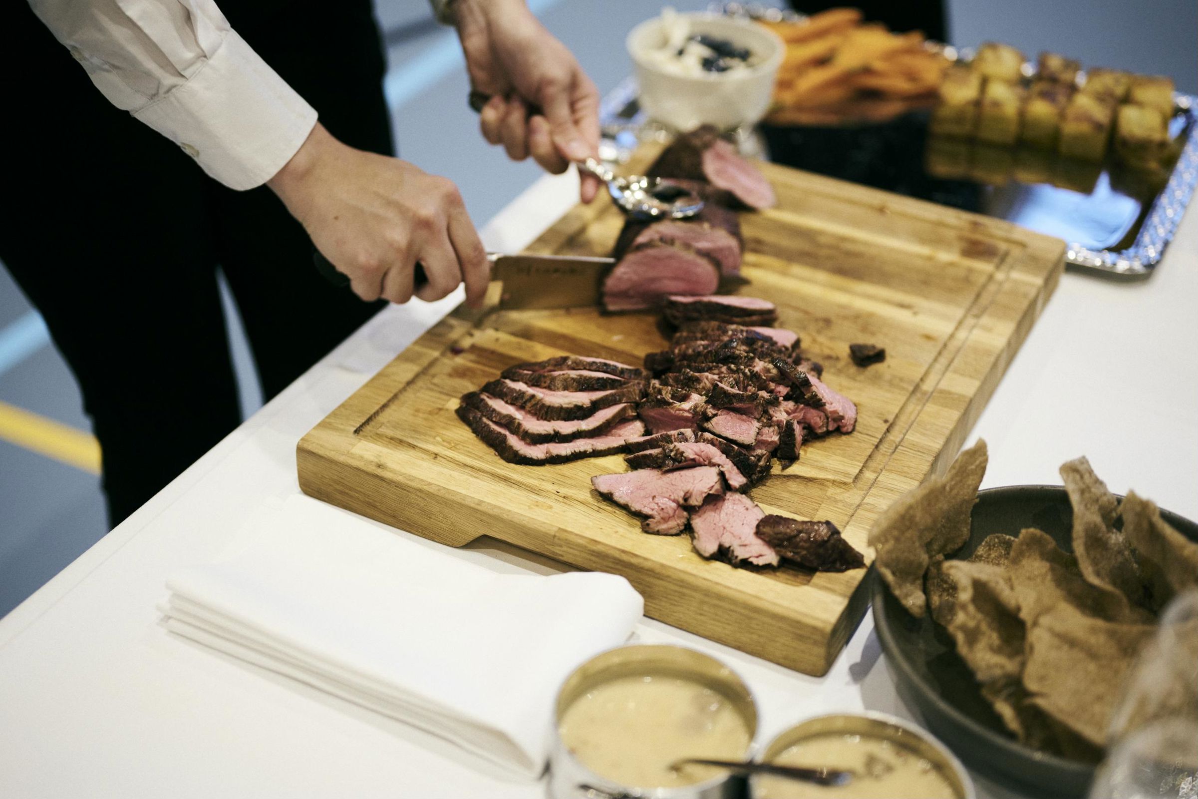 En tjenerelev trancherer en mør oksesteg ude ved gæsterne, inden den serveres.