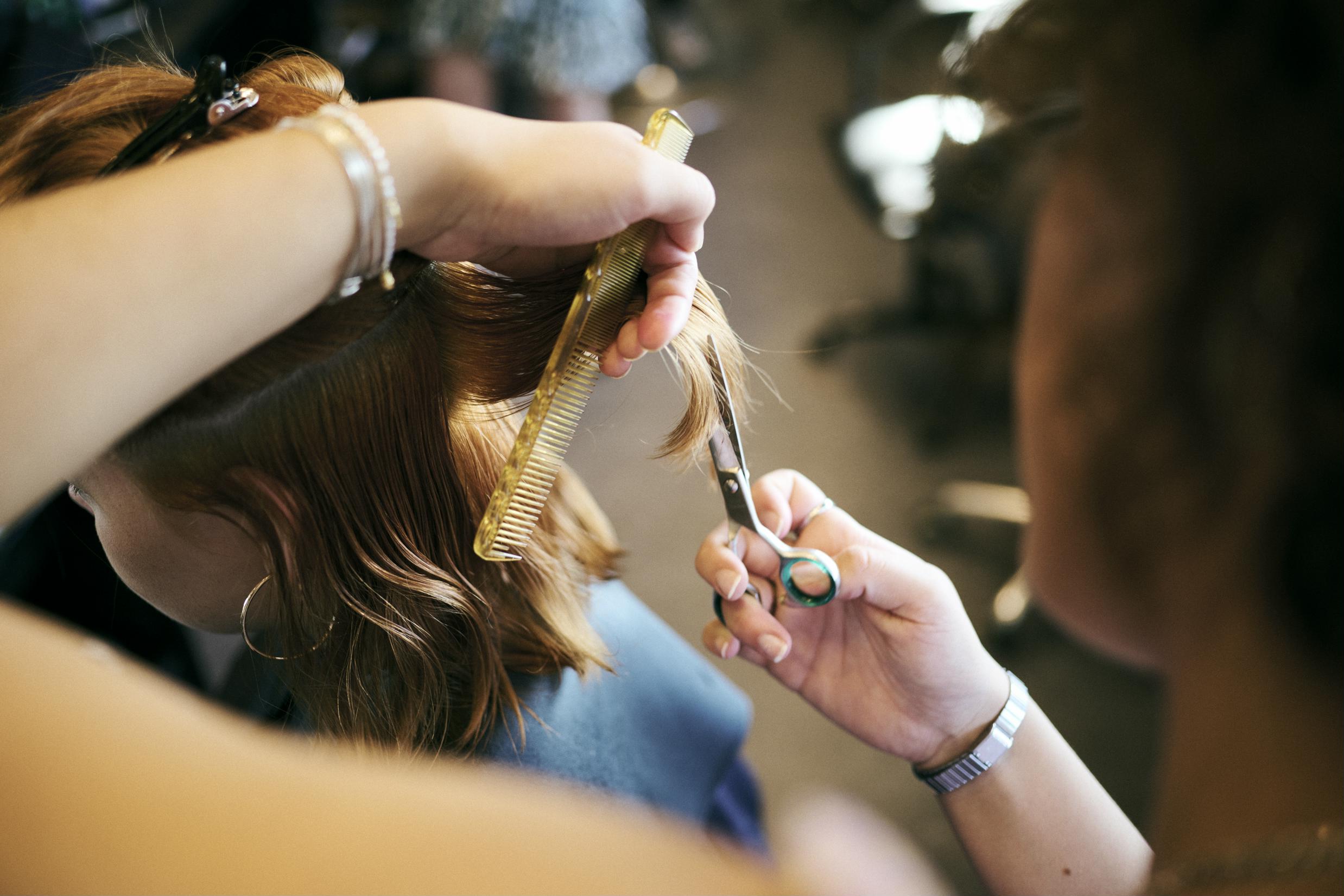 En pige sidder model og får klippet hår af en frisørelev på Hansenberg.