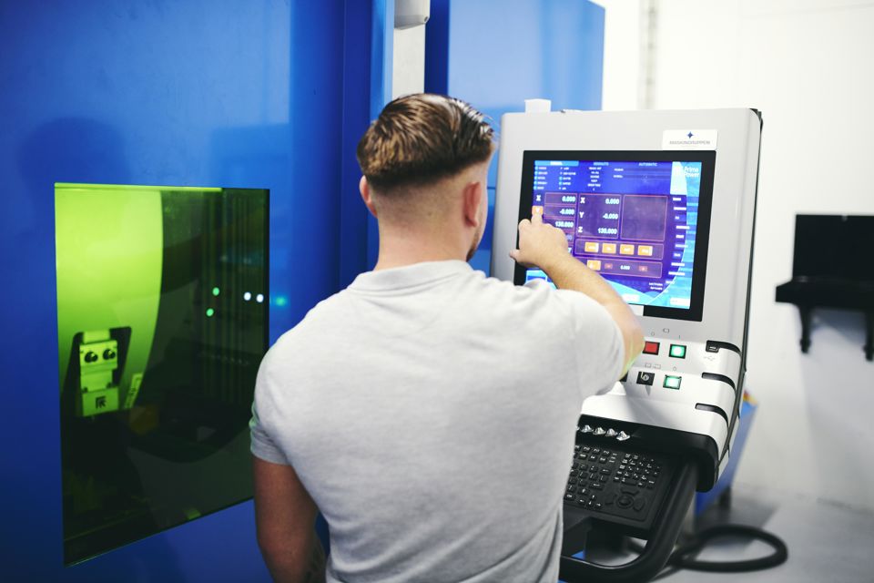 En smedelærling programmerer den store fiberlaser på Hansenbergs smedeværksted.