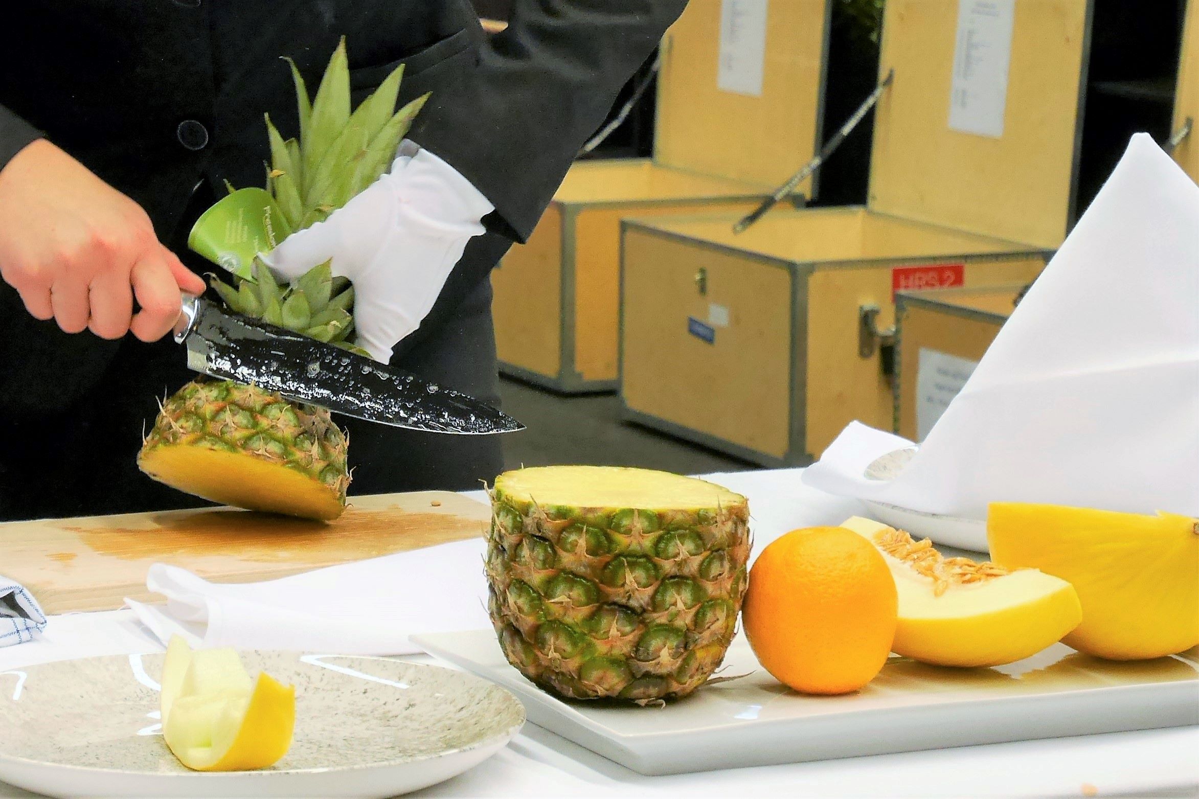 En tjenerelev skærer frugt uden af røre frugten med fingrene, her er det en ananas, der er under kniven.